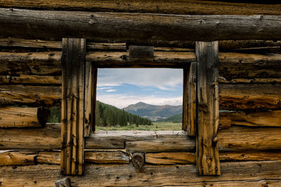 Wooden log cabin against sky and mountain landscape seen through the window 