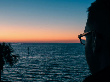 Silhouette person on sea against clear sky during sunset