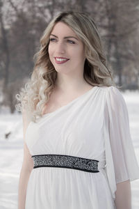 Smiling young woman looking away while standing on snow covered field