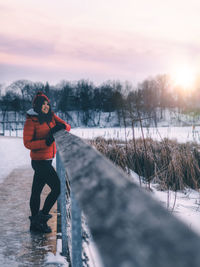 Woman standing in snow against sky during sunset