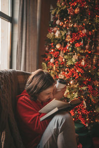 Portrait of candid authentic smiling boy teenager reading book on distance studying at home xmas