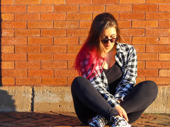 Young woman wearing sunglasses against brick wall