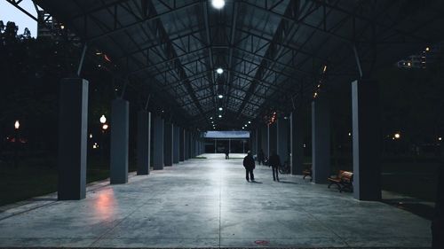 Man walking on illuminated footpath amidst buildings in city at night