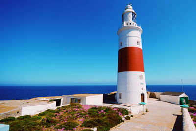 Lighthouse by sea against clear blue sky