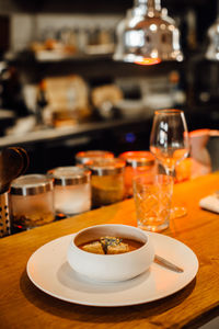 Plate of soup and glasses on bar counter at open kitchen restaurant