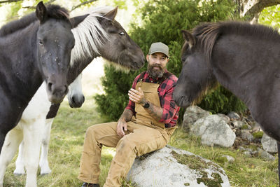 Male farmer sitting among horses