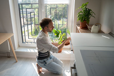 Young man wearing back support belt taking care of houseplants at home