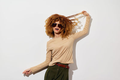 Portrait of young woman with arms raised standing against white background