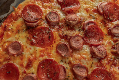 Macro photography of pepperoni and sausage pizza on metal tray with a black napkin in a wooden table