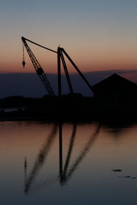 Silhouette cranes by lake against sky during sunset
