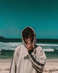 Portrait of young man smoking at beach against clear sky