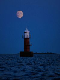 Lighthouse by sea against clear sky