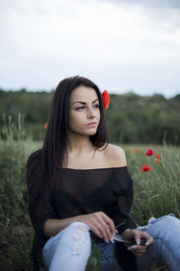 Thoughtful young woman sitting on field against sky