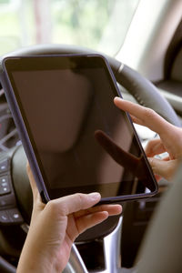 Cropped image of woman using digital tablet in car