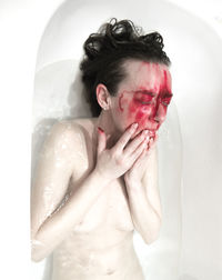 Sensuous naked woman with spooky face lying in bathtub