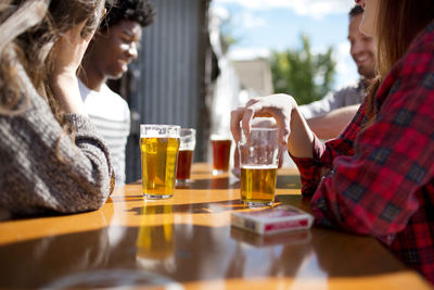 Friends having beer at table in brewery on sunny day