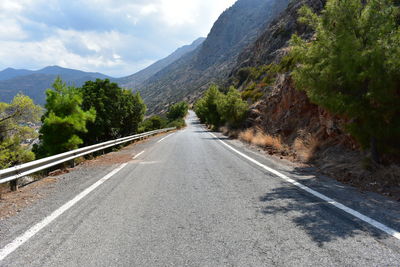 Empty road along trees and mountains against sky