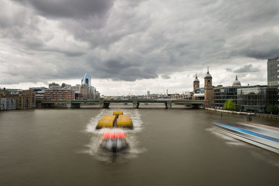 Bridge over river by buildings in city against sky
