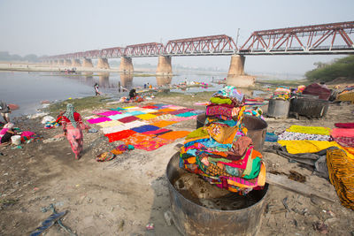 People washing and drying clothes at riverbank against bridge
