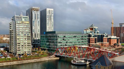 Modern buildings by river against sky in city