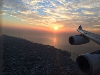 Airplane flying over cityscape against sky during sunset