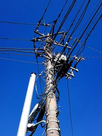 Low angle view of electricity pylon against blue sky