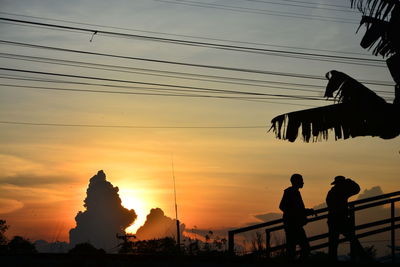 Silhouette people on bridge against sky during sunset