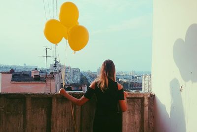 Rear view of woman holding balloons on balcony