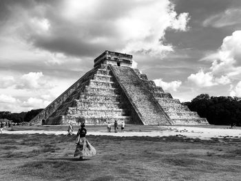 People standing by historical building against cloudy sky