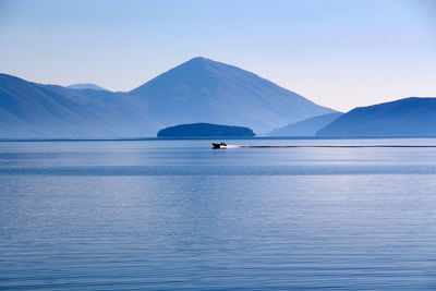 Distant view of boat sailing on lake against mountains