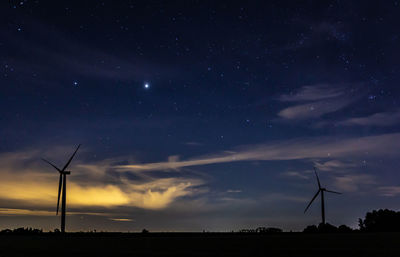 Low angle view of windmills on field against sky