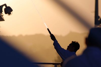 Man holding firework against orange sky