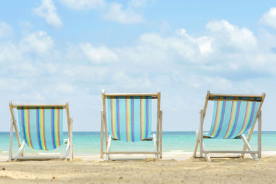 Deck chairs on beach against sky 