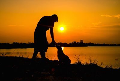 Silhouette men standing on shore against orange sky