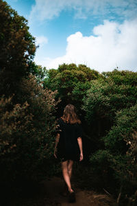 Rear view of woman walking in forest against sky