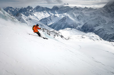 Off-piste skier on a glacier going down a beautiful alpine landscape. blue cloudy sky in the