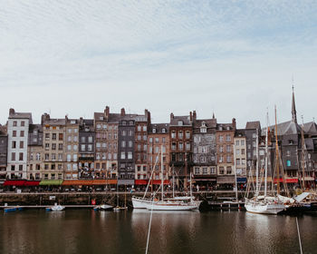 Boats moored in river by buildings in city against sky