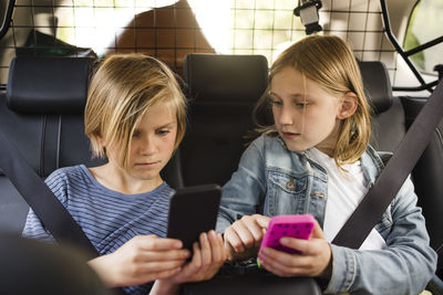 Blond siblings using smart phones while sitting in car