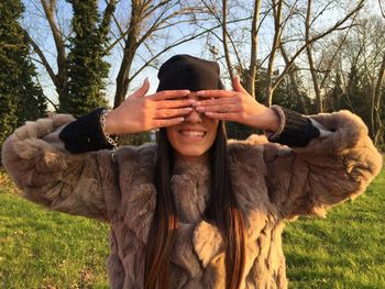 Mature woman covering eyes while standing against trees in park during sunset