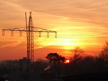 Silhouette electricity pylon against dramatic sky during sunset