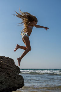 Full length side view of girl in bikini jumping from rock into sea