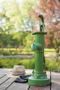 Old green manual water pump in a sunny garden with straw hat and gloves