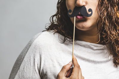 Midsection of woman holding mustache against wall