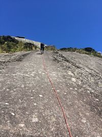 Low angle view of man climbing on mountain against clear blue sky