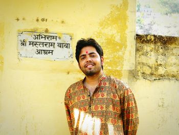 Portrait of smiling young man standing against wall