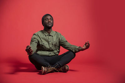 Portrait of young man sitting against red background