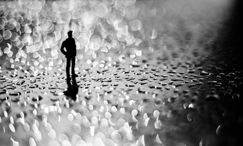 Rear view of silhouette man standing against illuminated lights