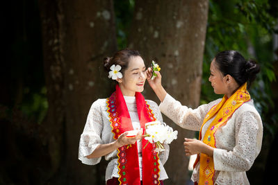 Young woman wearing flowers to friend while standing in park