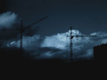 Low angle view of silhouette crane against cloudy sky at dusk