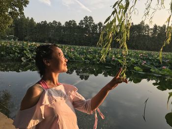 Smiling woman looking away while standing by lake against sky